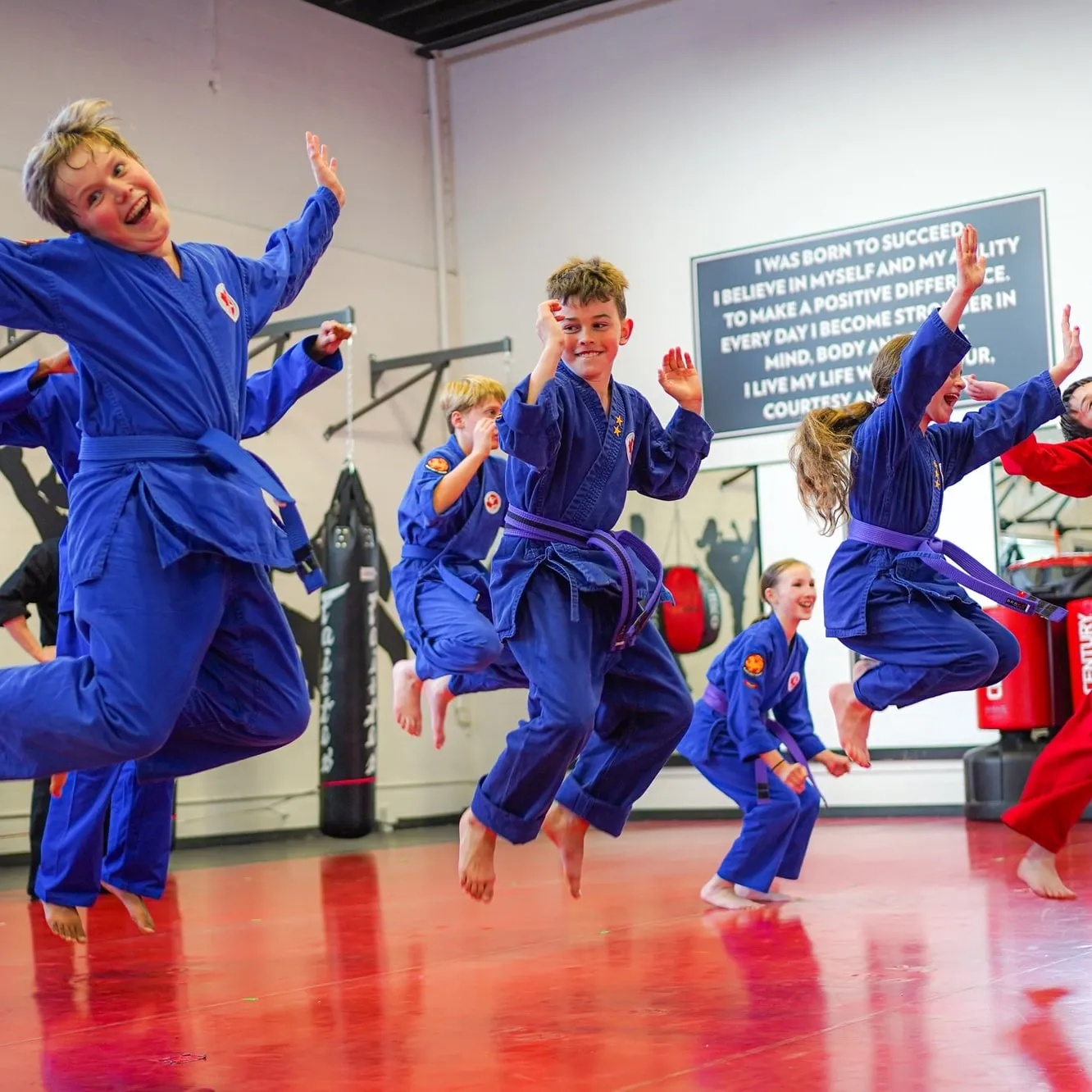 Kids in blue karate uniforms jumping and cheering on the red mats at Safeguard