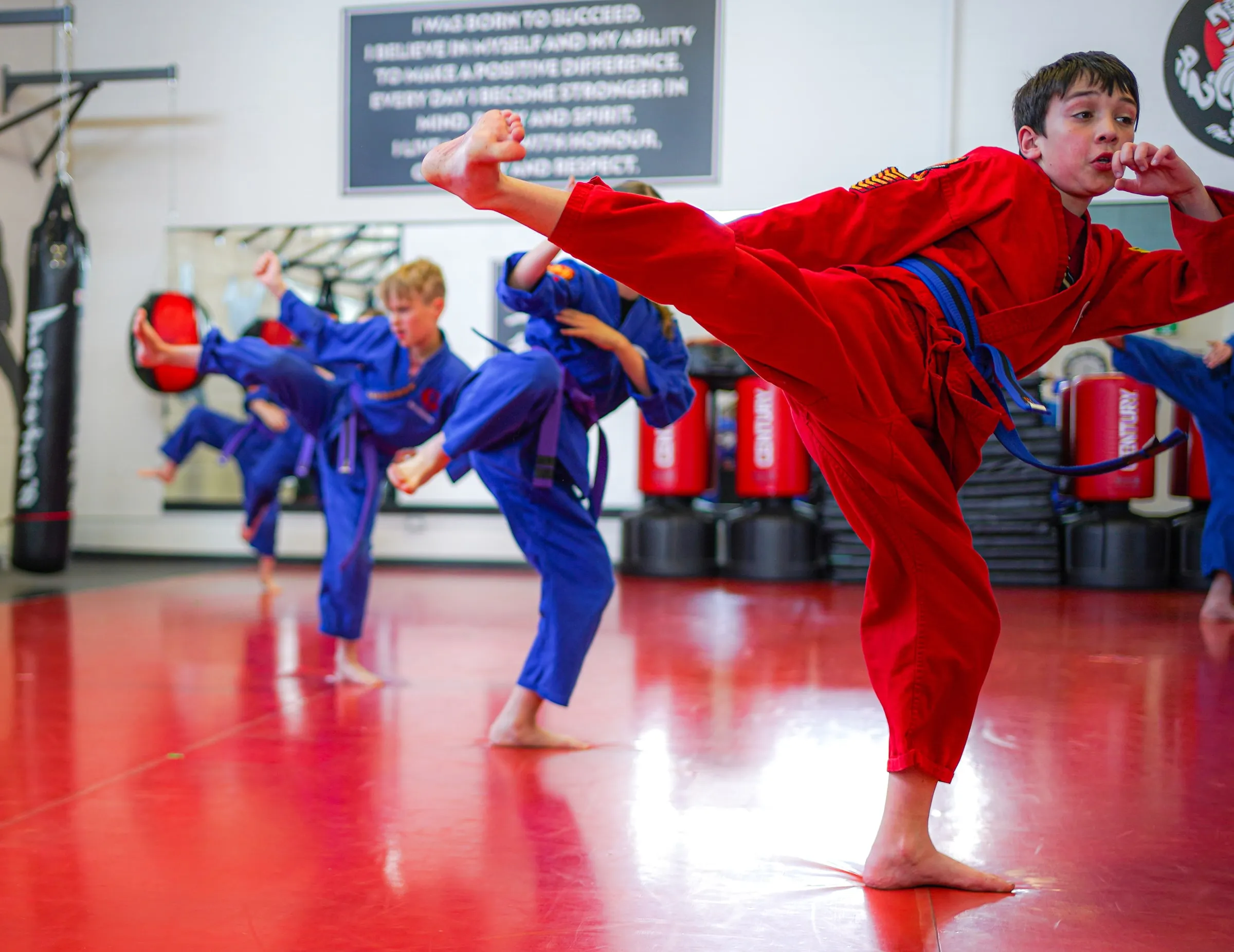 A junior student in a red uniform throwing a high kick