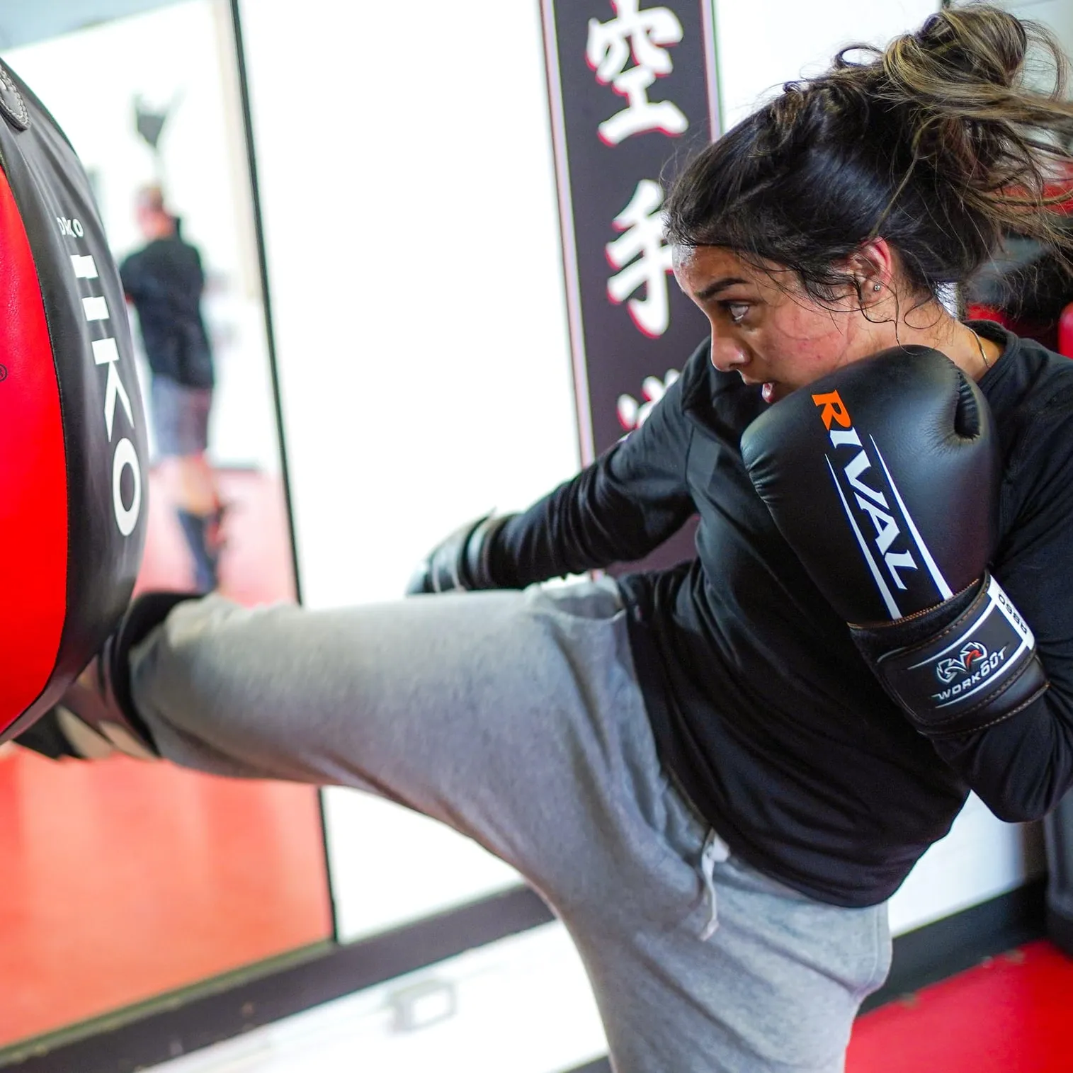 An adult kickboxer driving a kick into a red pad