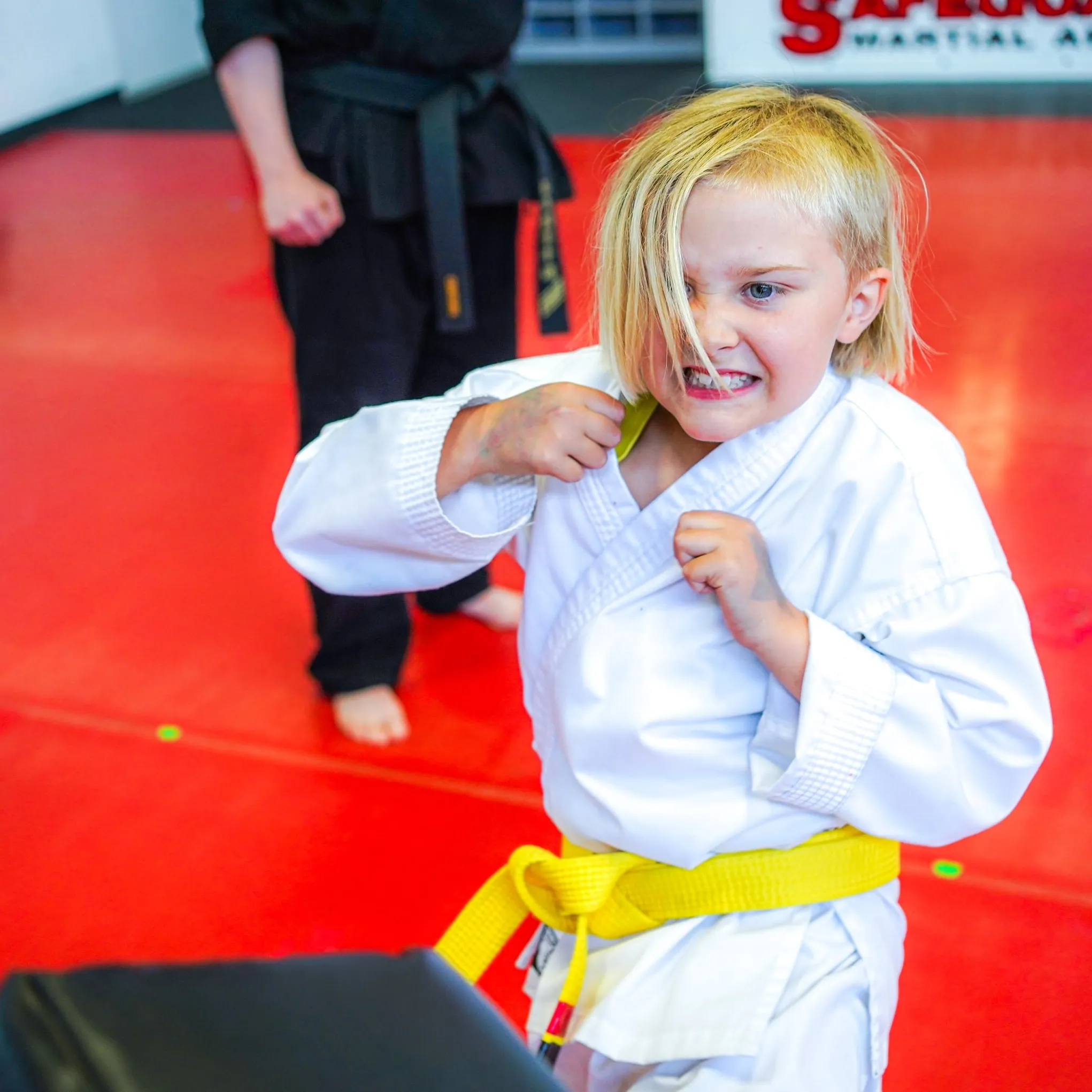 A young yellow belt throwing a punch with a fierce grin