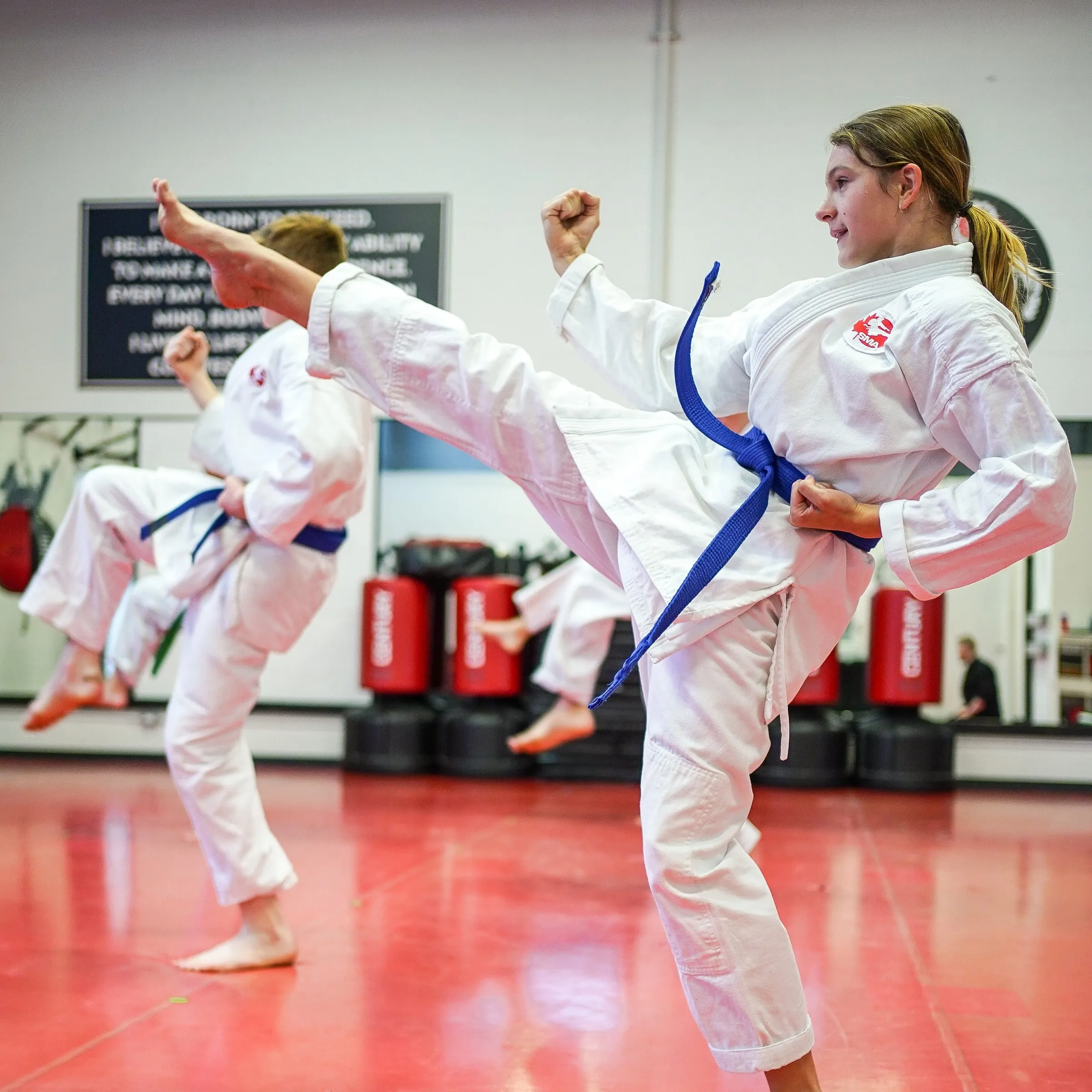 A blue belt throwing a front kick in the teen and adult karate class